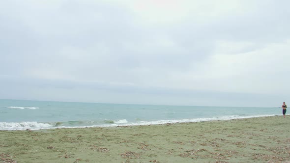 Stormy Seaside, Gray Clouds on Horizon. Young Brunette Female Running on Beach