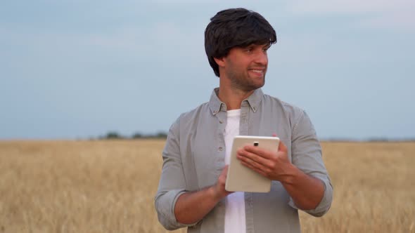 Man Farmer Using Digital Tablet Computer Standing in a Wheat Field and Using Apps and Checking