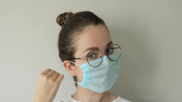 Portrait of Woman Putting Off Mask From Face and Smiling on Grey Background.