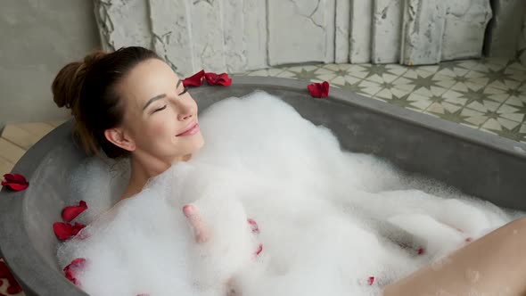 Girl Lies in a Large Stone Bath in Foam