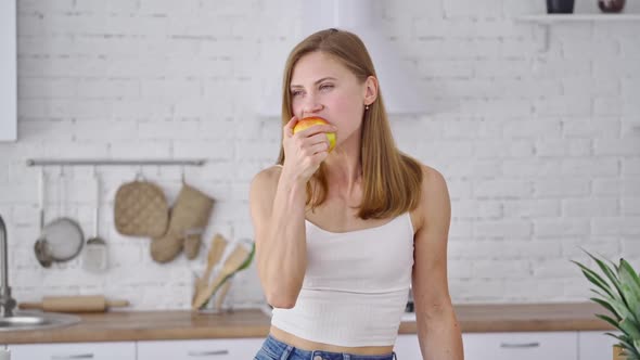 Beautiful woman eating tasty apple indoors. Young female with sporty body