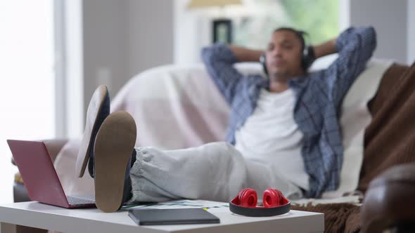 Closeup of Feet in Slippers and Pajama Pants on Table with Blurred African American Young Man in