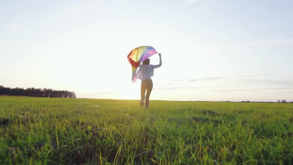 Young Positive Woman Runs Across Field with LGBT Flag Slow Mo Rear View
