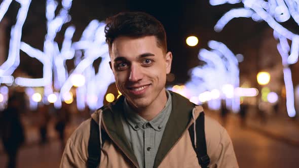 Portrait of Positive Brunette Guy 20s Smiling in Slow Motion While Walking Through Night City with