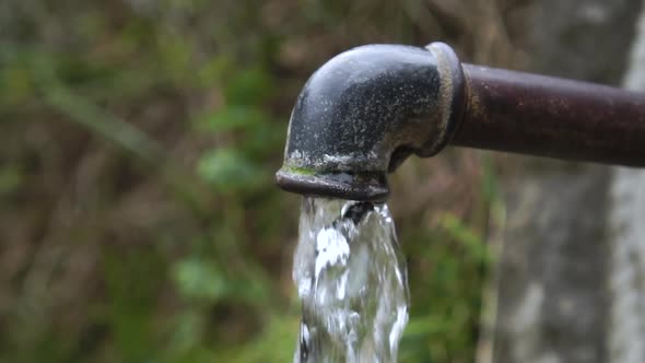 Tap water pours from a rusty iron pipe in the garden