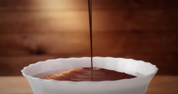 Closeup Hot Melted Liquid Chocolate Flows in White Bowl on Wooden Background in Kitchen Pouring