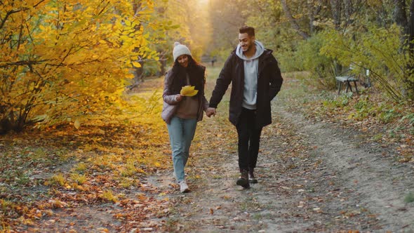 Young Hispanic Happy Couple in Love Walking Outdoors Going in Autumn Woods in Sunshine Enjoying