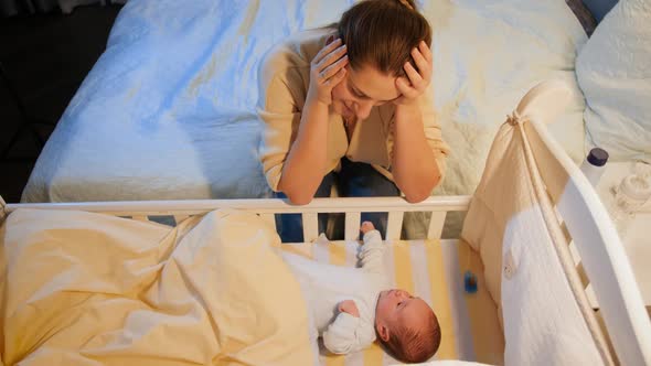 Exhausted Young Woman Rocking Crib of Her Sleepless Newborn Baby