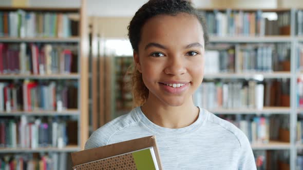 Portrait of Attractive African American Student Holding Books in Library Smiling