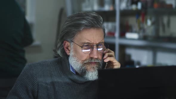 Mature Designer Reading Data From Computer During Phone Conversation