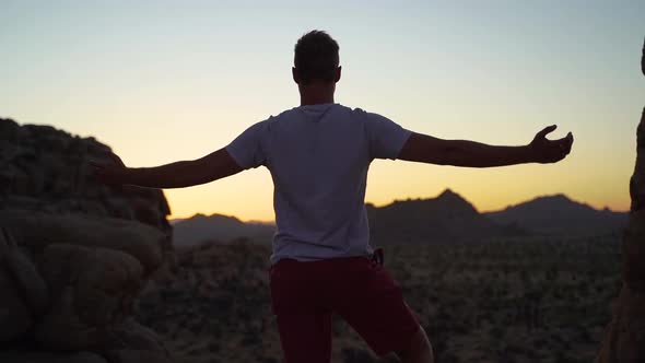 Man raising his arms after long hike, sunset at Joshua Tree, California, slow motion shot