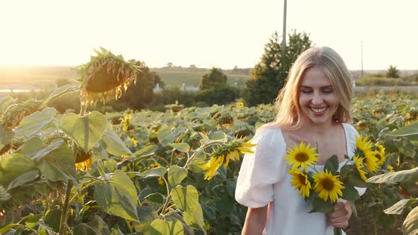 Girl Smells Bouquet of Sunflowers in the Field in Sunrays