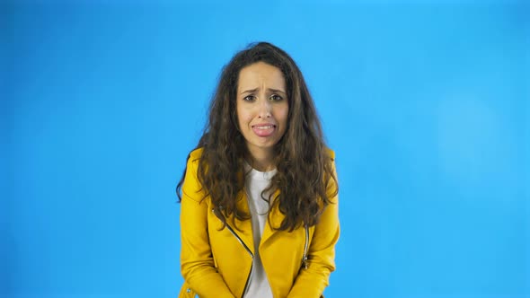 Confused Young Woman in Yellow Jacket in Studio with Blue Background.