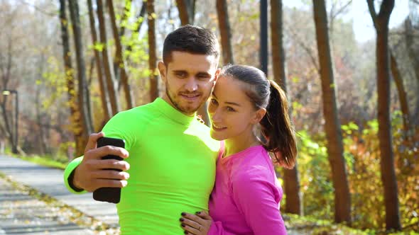 Smiling Athletic Couple in Sportswear Taking Selfie Photo in Autumn Park