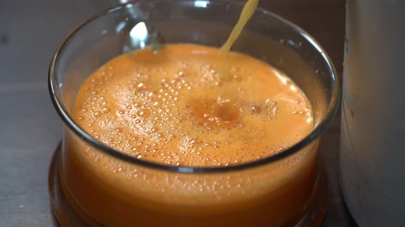 Fresh carrot and orange juice poring down into glass bowl from juice machine - Slow motion