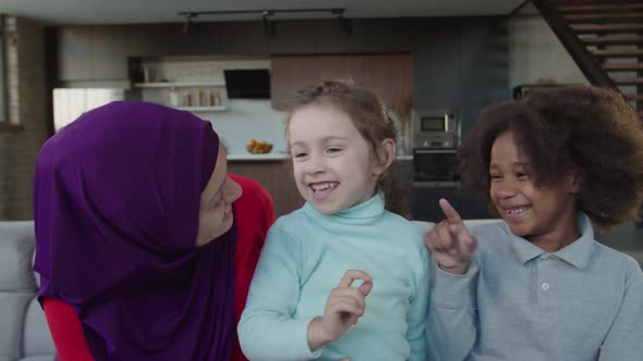 Carefree Pretty Hijab Arab Mother Having Fun with Two Multiracial Little Daughters at Home