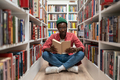 Student african american man reading research textbook in university library sitting on floor. - PhotoDune Item for Sale