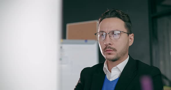 Closeup Portrait of a Businessman Wearing Glasses Sitting in His Office in Front of a Monitor