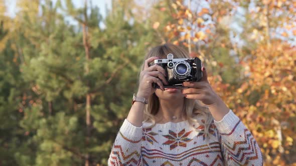 Blonde Girl Takes Pictures on a Retro Camera in a Park