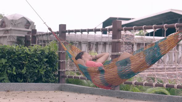 Young Woman with Dark Brown Hair Lies in Hammock on Resort