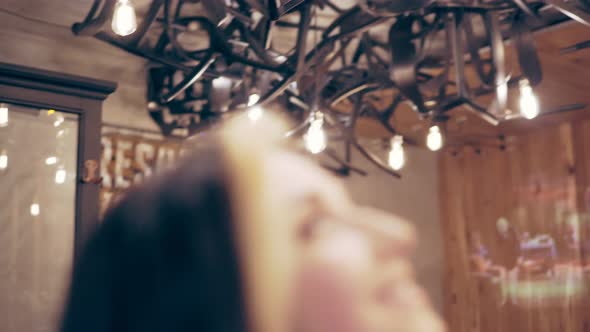 Young Brunette Woman Touches the Decorated Lamps and Turns to Camera Smiling
