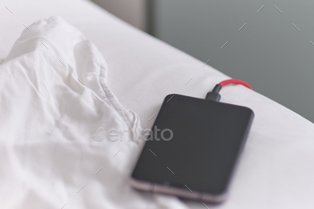 Smart phone is charging on the bed and lying on white fabric.