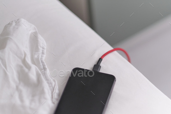 Smart phone is charging on the bed and lying on white fabric.