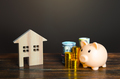 Piggy bank and coins near a house. Savings on home bills, energy saving technologies.  - PhotoDune Item for Sale