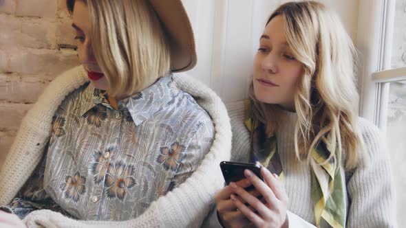 Two Young and Beautiful Girls Sitting in Cafe and Using Phone Blogger