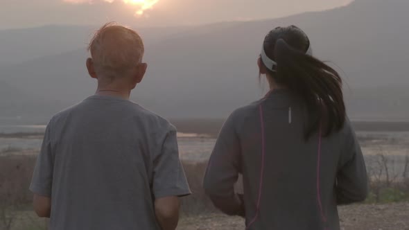 Grandfather and granddaughter are jogging by the lake at sunset and tell stories of past life