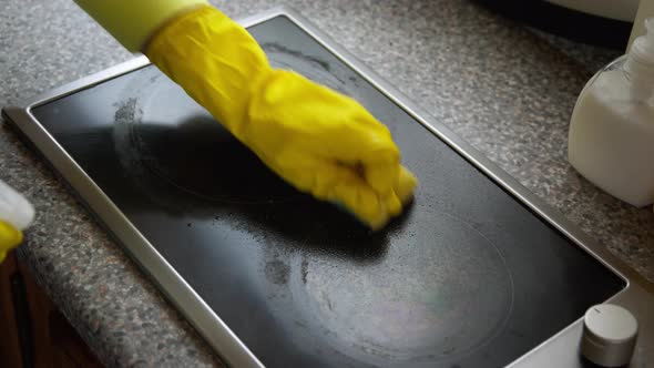 Woman Hand in Yellow Rubber Gloves Washes Induction Stove Using Spray Detergent