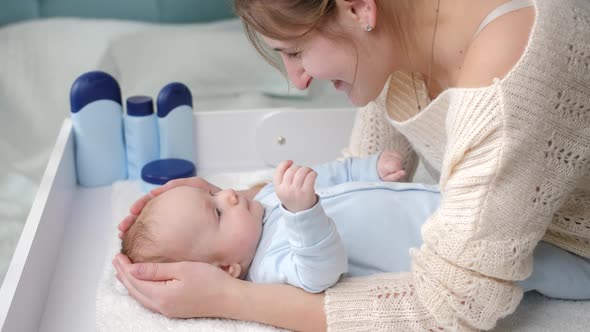 Smiling Mother Stroking and Smiling at Her Little Baby Boy Lying on Dressing Table at Bedroom