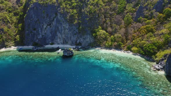 Aerial View of Filipino Boats Floating in Blue Lagoon on Top of Coral Reef in Front of Huge Cliff