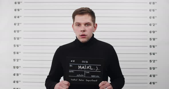 Portrait of Young Man in Black Turtleneck Holding Sign for Photo in Police Department