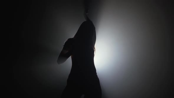 Slim Sexy Woman Dancing on Smoke Dark Stage in Front of Light Projector. 