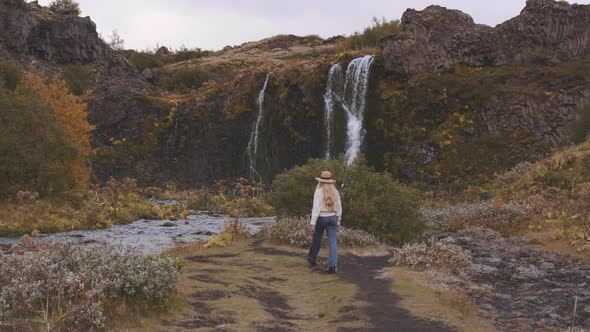 Woman Walking Towards Waterfall