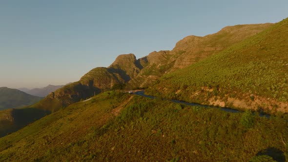 Aerial View of Road Traversing Mountain Landscape Lit By Bright Sun in Golden Hour