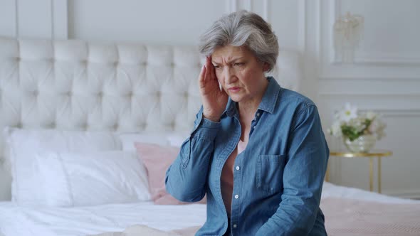 Older Woman Sit on Bed Coping with Headache 