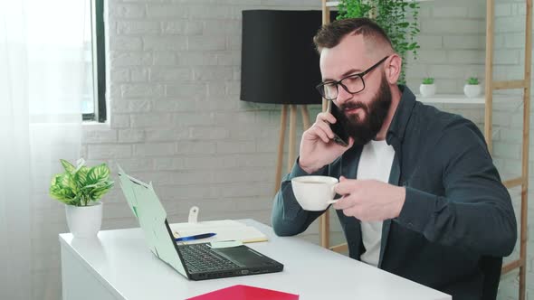 Handsome Bearded Man Drinking Coffee While Talking on a Smart Phone