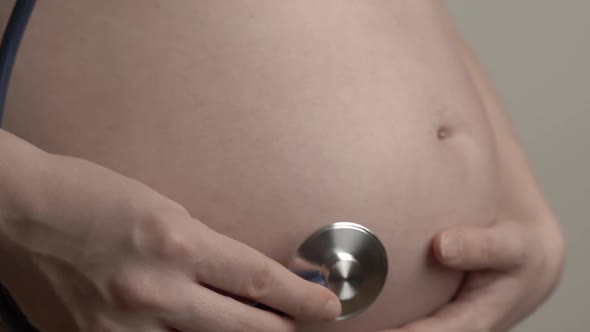 Pregnant Woman Listens to the Baby Heartbeat and Movements with a Stethoscope or Fetoscope or Pinard