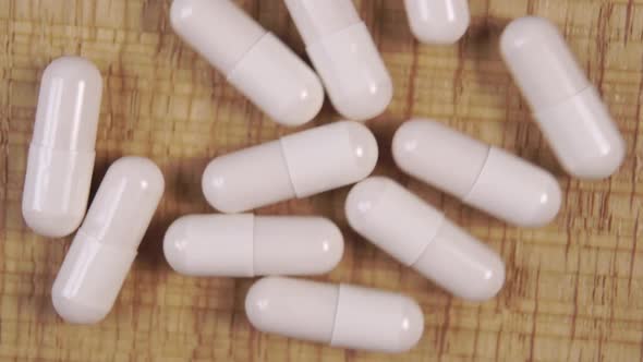 Slow drop of white medical capsules on a wooden table. 