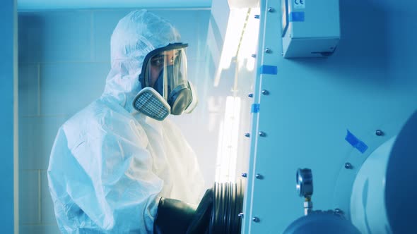 Laboratory Worker in a Hazmat Suit is Operating a Vacuum Cabinet