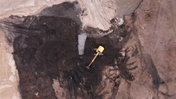 Excavator digs the ground at a construction site. Aerial top view.