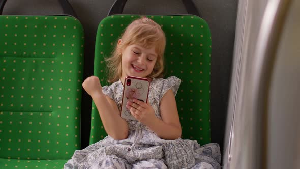 Child Girl in City Bus or Tram Transport Use Mobile Cell Phone Sincerely Rejoicing Win Good News alt