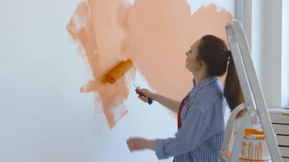 Singleton Lifestyle Concept. Young Happy Woman Paints Her Walls Orange with a Roller