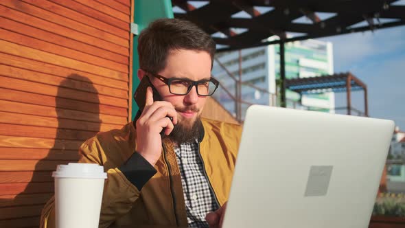 Man Talking on the Phone and Working on Laptop.