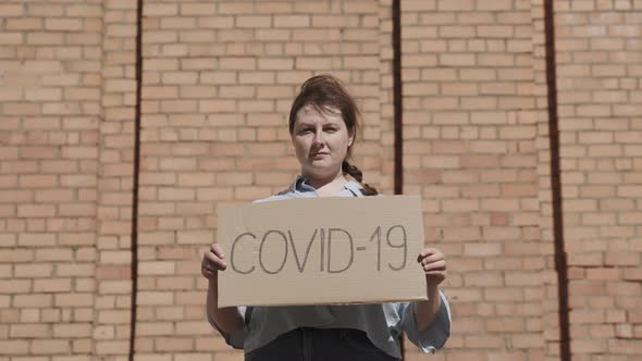 Portrait of Woman Holding Cardboard Sign COVID19 Monkeypox Near Brick Wall