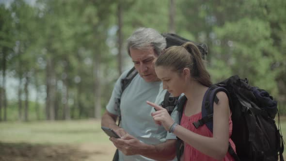 Father and daughter navigating in woods using smart phone