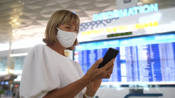 Caucasian Woman in a Face Mask Checking Her Flight with the Schedule on a Departure Board