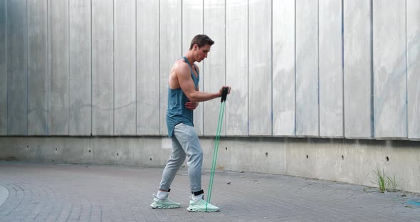 Young Athletic Man Using an Expander to Train Biceps Outdoors